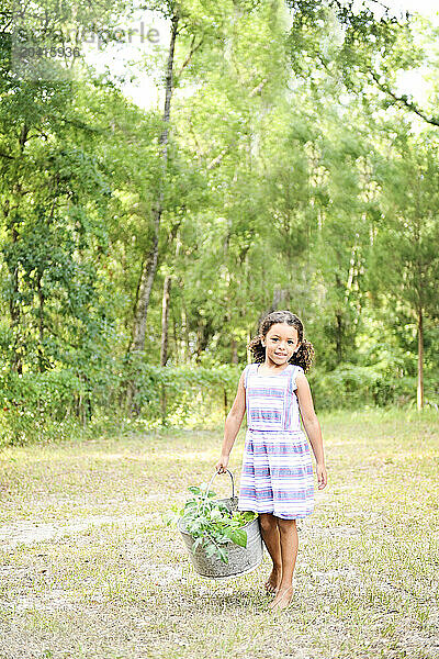 Young girl smiling holding a basket of harvested vegetables outdoors.