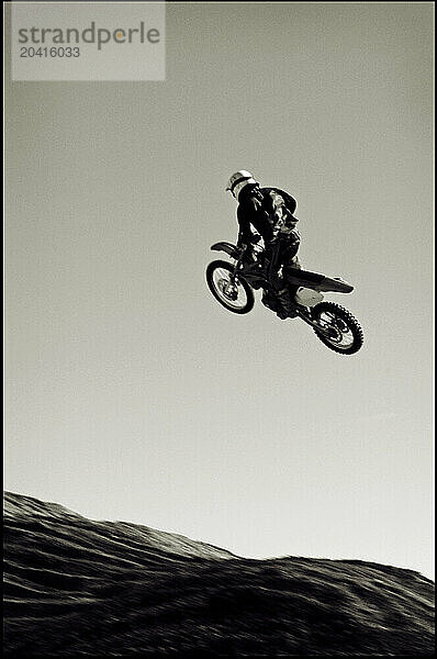 A young man jumps his dirt bike high in the air while motocross riding the surreal dunes near Cameron  AZ.