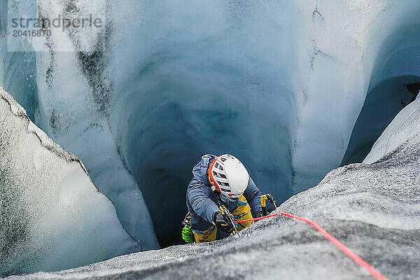 Man ice climbs inside a dark deep crevasse on an Icelandic glacier