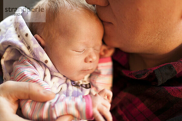 A father kisses his newborn baby as he holds her in his home.