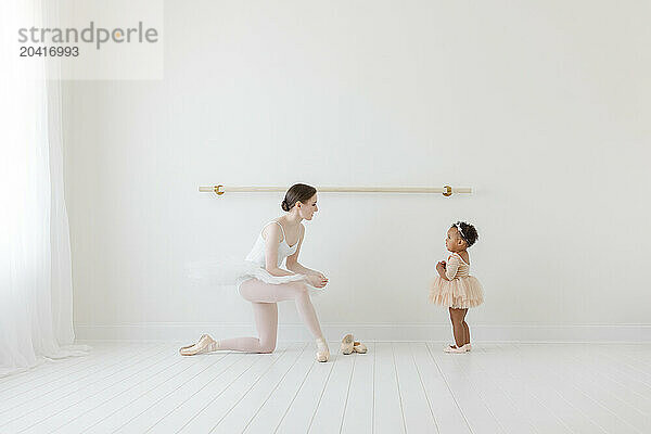 Adult Ballerina shows BIPOC baby ballet barre in white studio