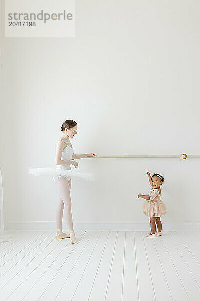 baby ballerina points to ballet barre in white studio