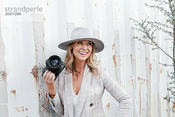 Woman holding camera smiling by rustic wall