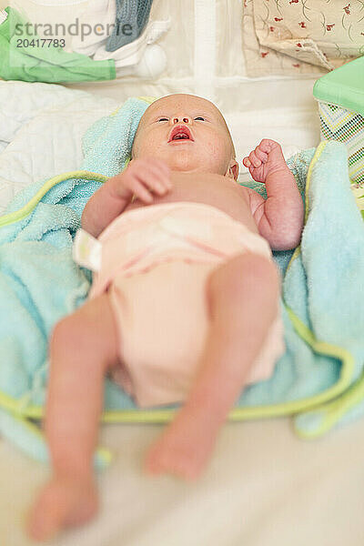 A newborn baby in a pink diaper lies on it's back on a changing table.