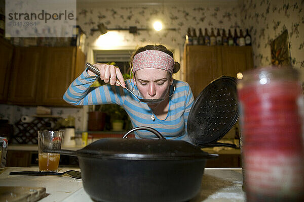 Young woman tasting soup in kitchen.