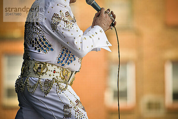 Elvis impersonator holding a microphone on stage performing in front of a crowd.