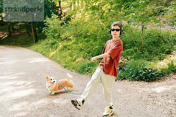 teenage boy in headphones dance and plays with a corgi dog in summer