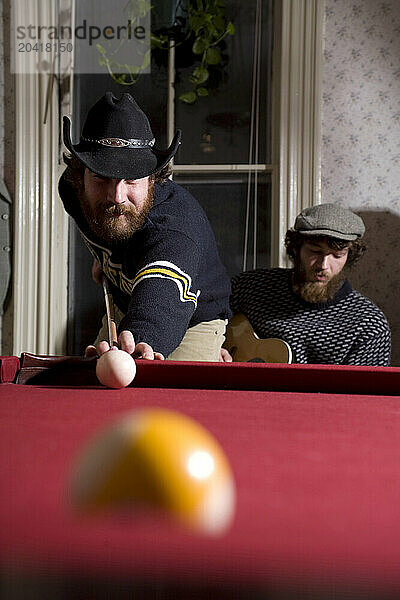 Young man with beard playing pool.