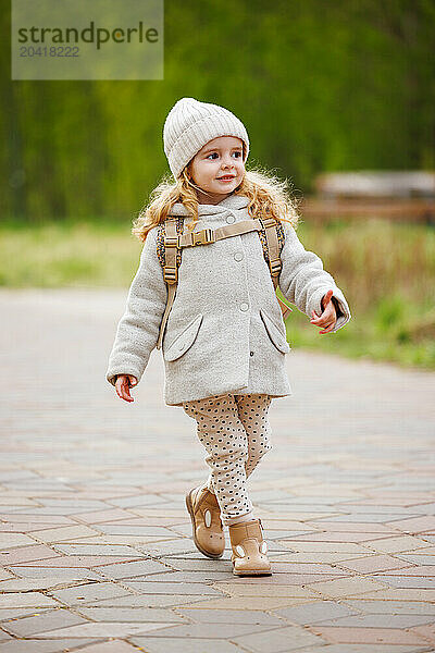 A happy girl in a coat strolls through the city park