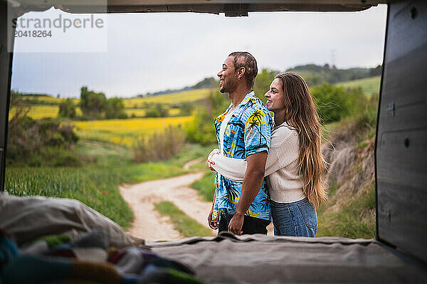 Happy diverse young couple standing near van rear door