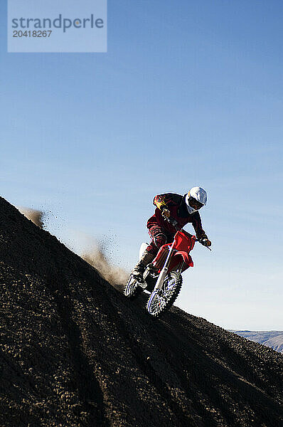 A young man lands after jumping his dirt bike high in the air while motocross riding the surreal dunes near Cameron  AZ.