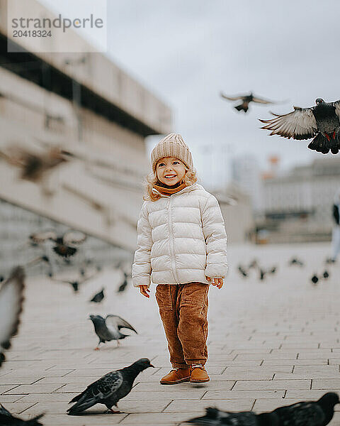 little girl  3-4 y ears old  stands on the pigeons square