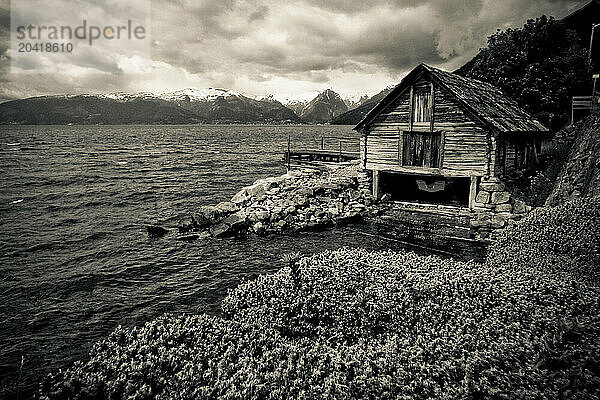 An old wooden building sits on the shores of a fjord in Norway.