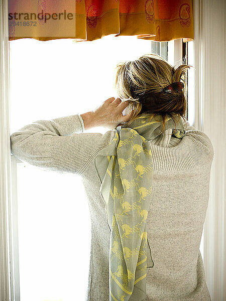 woman looks out window as she talks on the phone