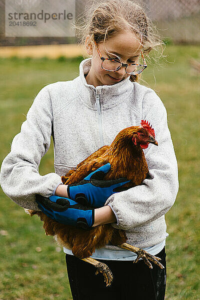 Girl with blond hair cradles a chicken in yard outside