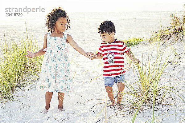 Two children holding hands while walking on a sandy beach  surro