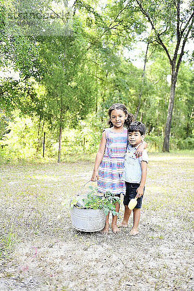 Happy siblings outdoors with a basket of harvested vegetables  smiling