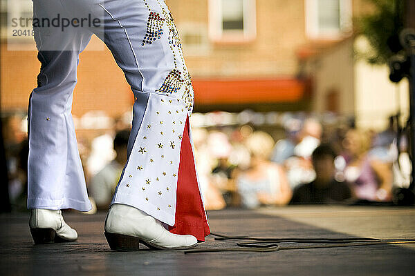 Elvis impersonator holding a microphone on stage performing in front of a crowd.