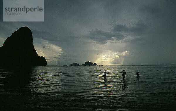 Swimmers are silhouetted against a stormy sky in Thailand's Railay West Beach.