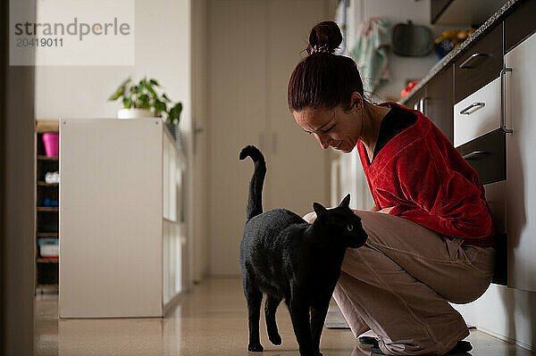 Woman with black cat in kitchen at home