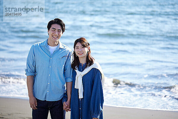 Japanese couple standing on the beach holding hands