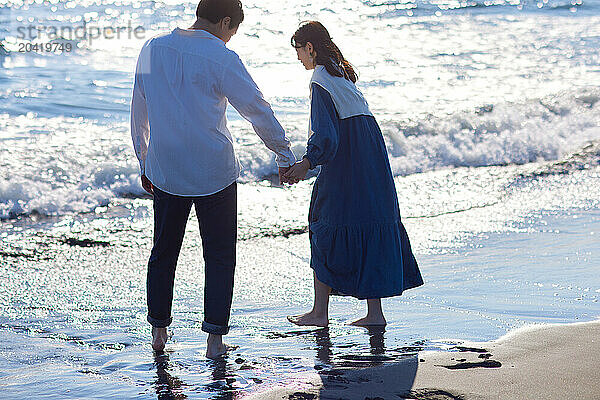 Japanese couple are holding hands while walking on the beach