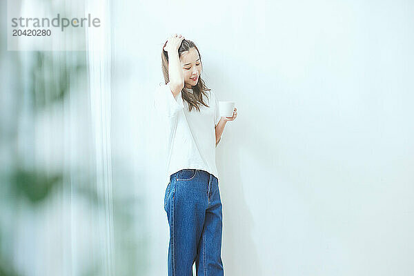 Japanese woman standing in front of a white wall holding a cup