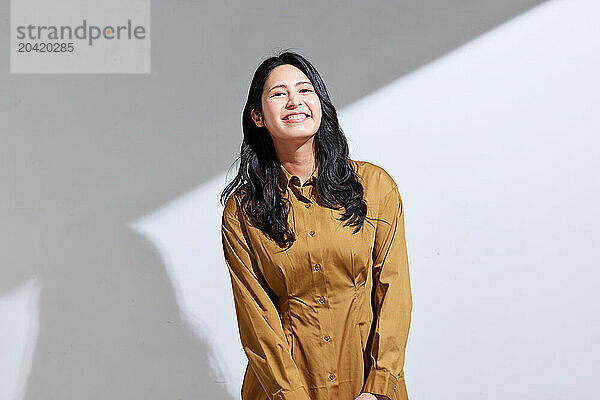 Japanese woman in a brown dress standing in front of a white wall