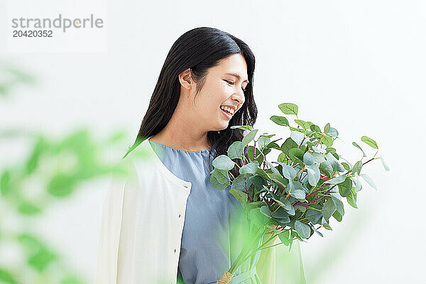 Japanese woman holding a plant against a white wall