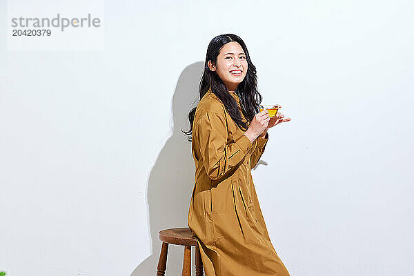 Japanese woman in a brown dress standing in front of a white wall