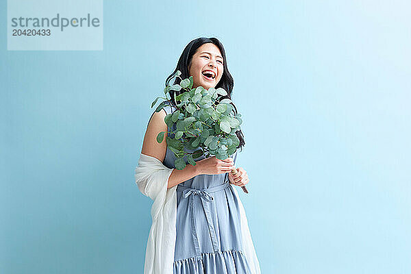 Japanese woman holding a plant against a blue wall