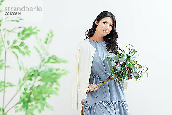 Japanese woman holding a plant against a white wall