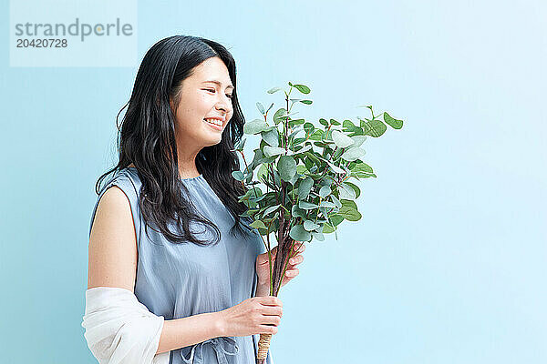 Japanese woman holding a plant against a blue wall