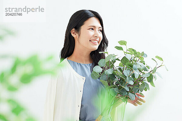 Japanese woman holding a plant against a white wall