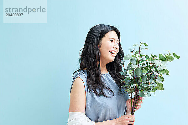 Japanese woman holding a plant against a blue wall