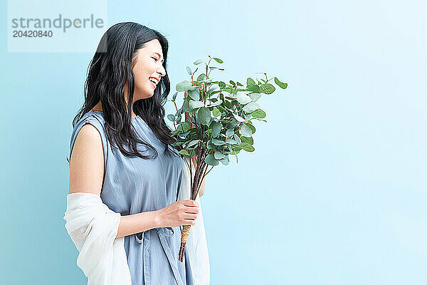 Japanese woman holding a plant against a blue wall