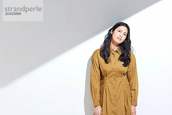 Japanese woman in a brown dress standing in front of a white wall