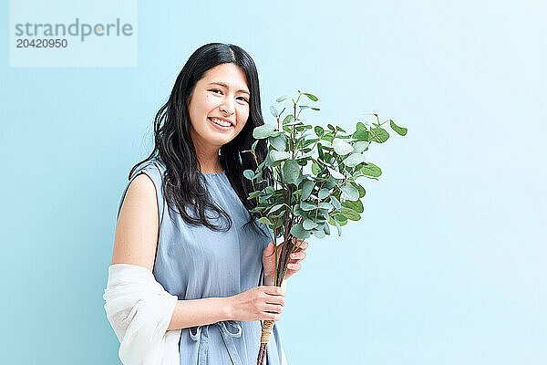 Japanese woman holding a plant against a blue wall