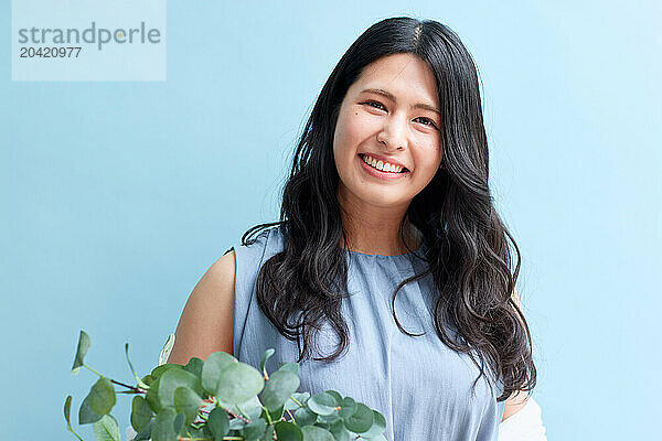 Japanese woman holding a plant against a blue wall