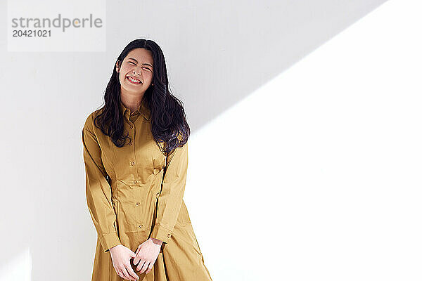 Japanese woman in a brown dress standing in front of a white wall