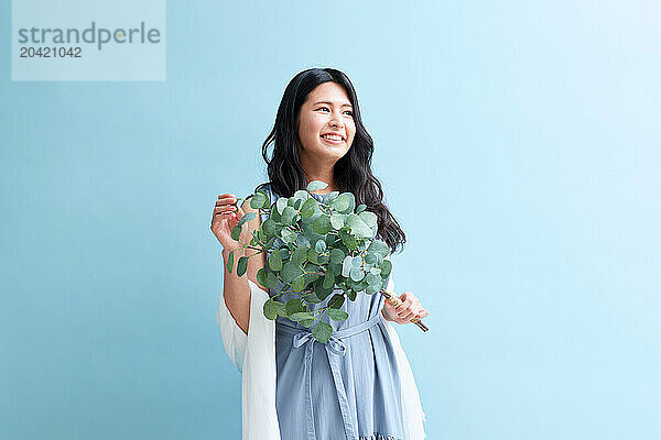 Japanese woman holding a plant against a blue wall