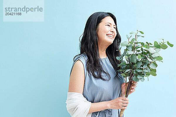 Japanese woman holding a plant against a blue wall