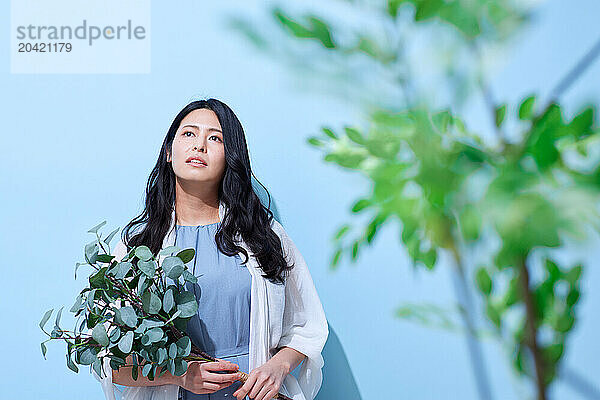 Japanese woman holding a plant against a blue wall