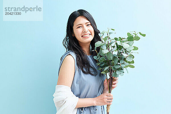 Japanese woman holding a plant against a blue wall