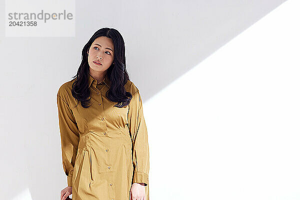 Japanese woman in a brown dress standing in front of a white wall