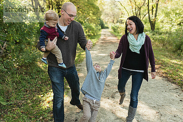 Happy parents swinging toddler son while holding hands in nature park