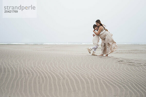 Young girl hugging her pregnant mother on a cloudy beach