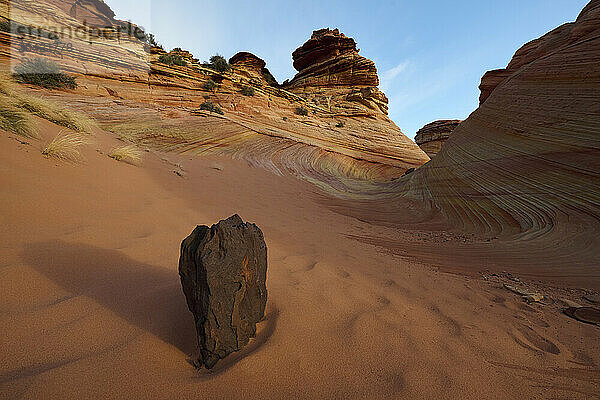 A lone rock in the sand in front of some wild rock formations in