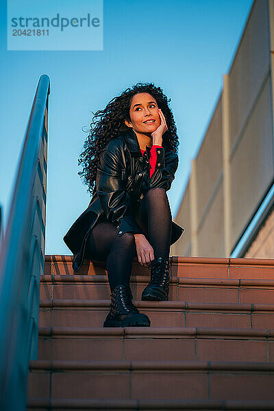 Curly-haired woman sitting on steps of building