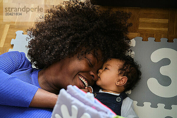 African woman is laying on the floor with a baby laughing.